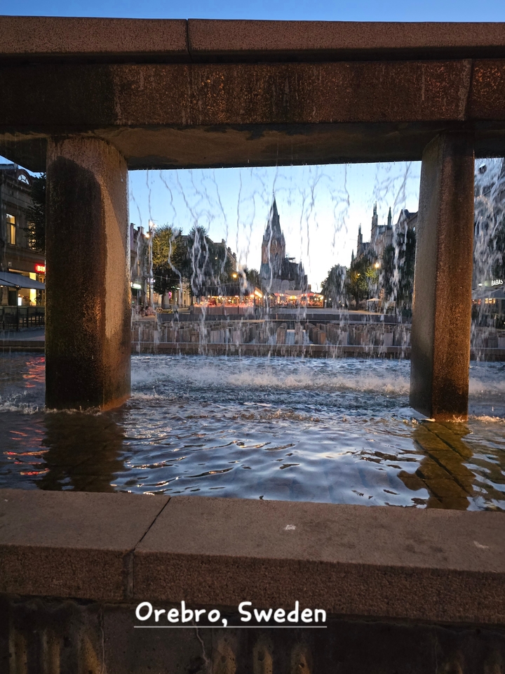 Vue de fontaine au crépuscule avec eau qui coule et environnement éclairé.
