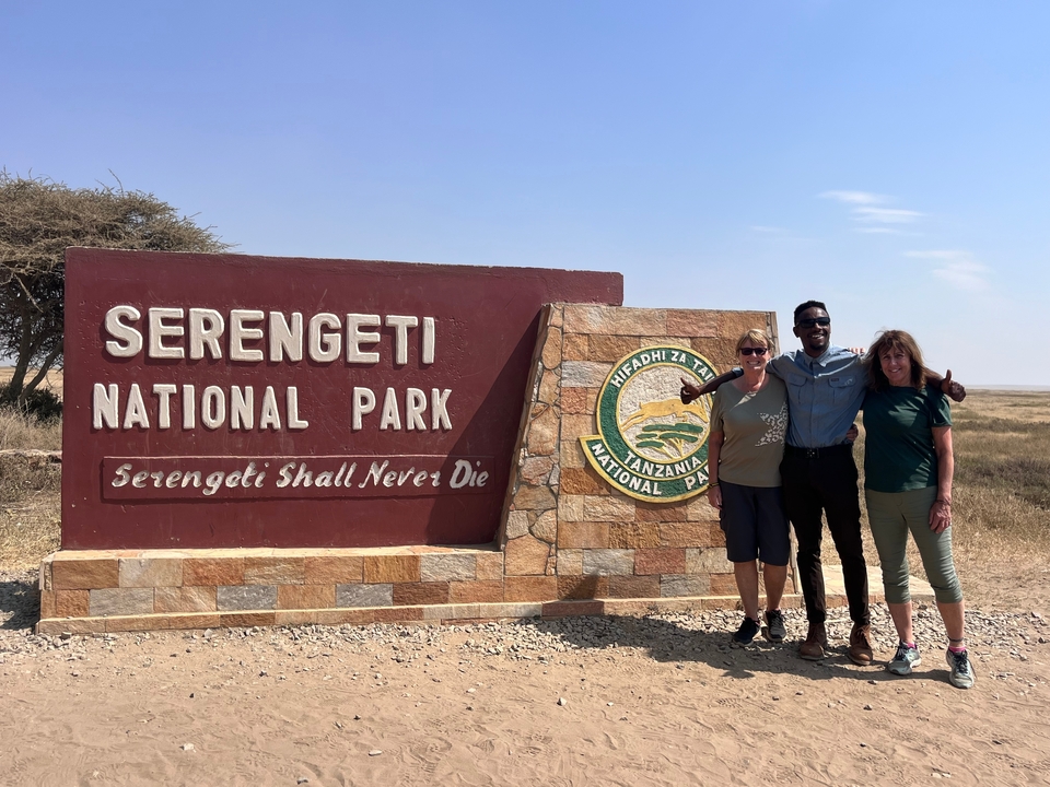 Trois personnes posant près du panneau du parc national du Serengeti.