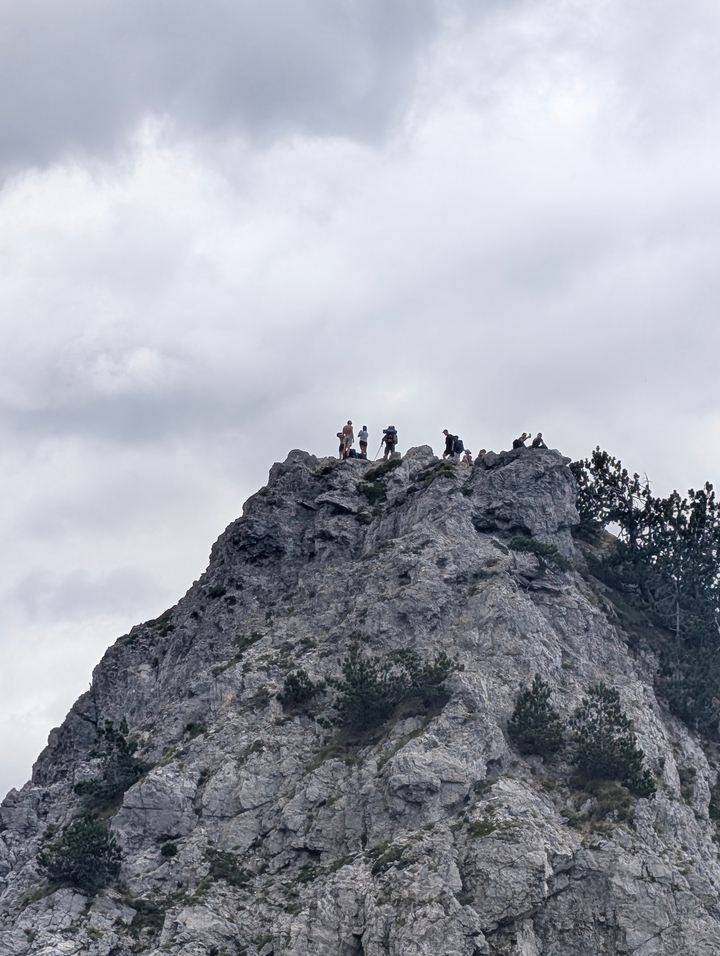 Randonneurs debout au sommet d'un pic rocheux avec un ciel nuageux