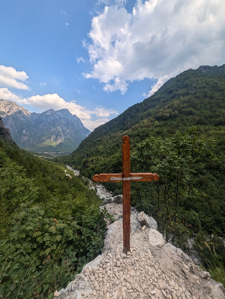 Croix en bois dans une vallée verdoyante avec de hauts sommets