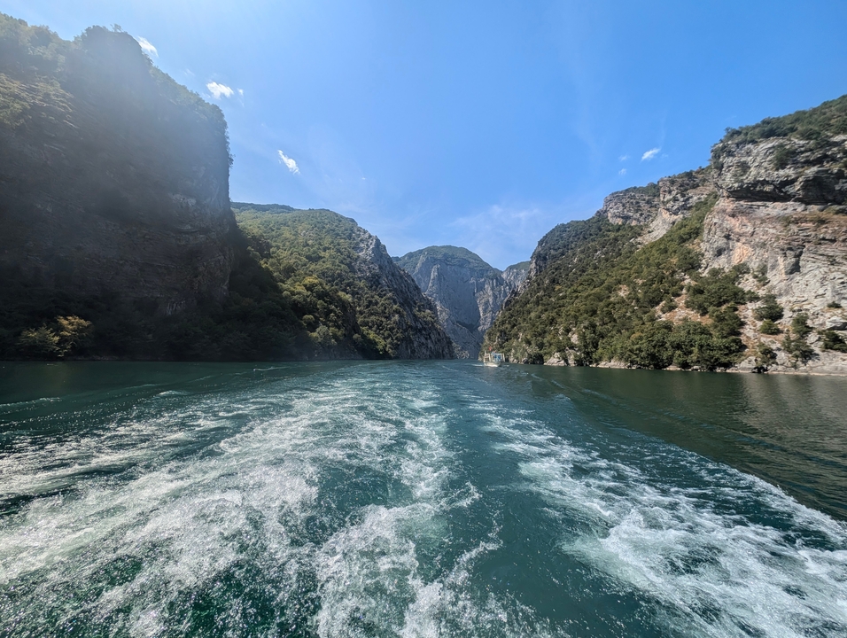 Sillage d'un bateau sur une rivière entre des falaises escarpées.