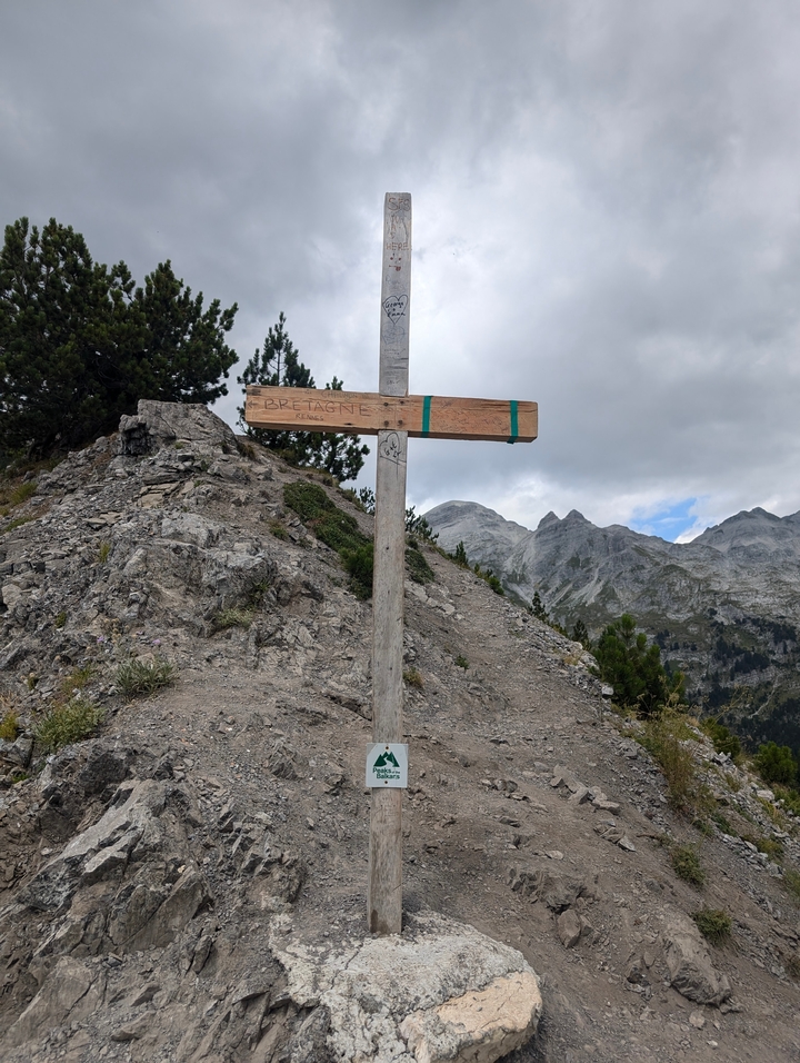Croix en bois sur un sommet rocheux avec un arrière-plan montagneux.