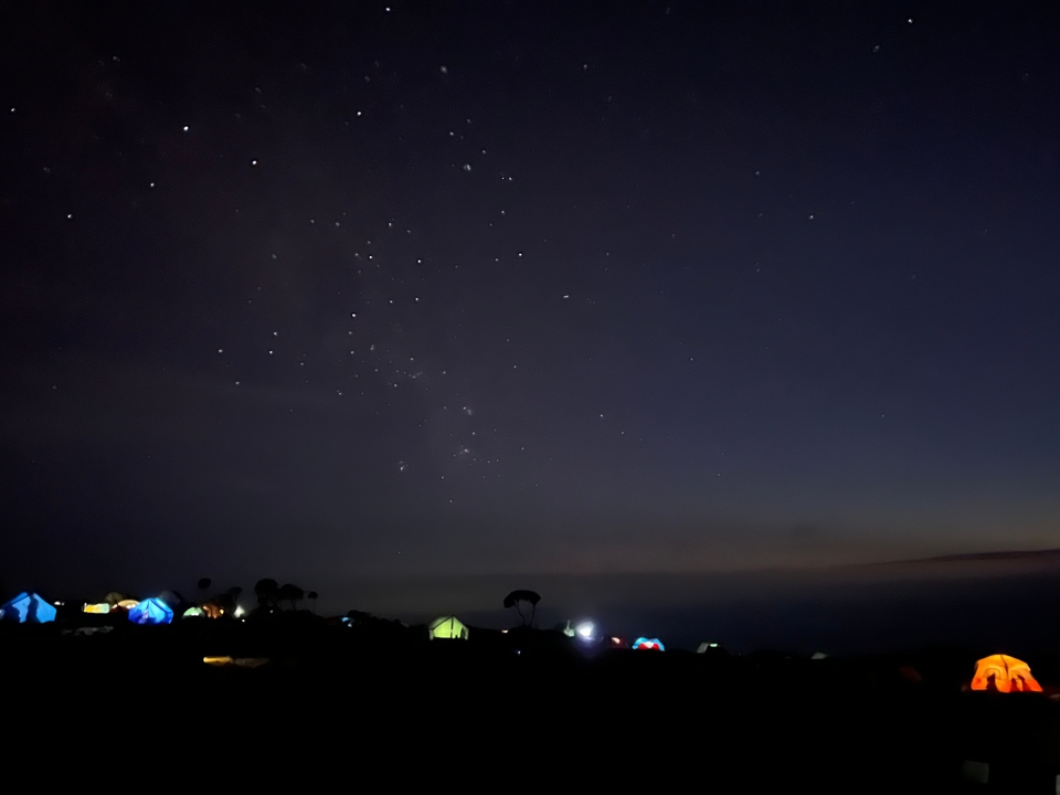 Ciel nocturne avec une vue des étoiles et des tentes en contrebas.
