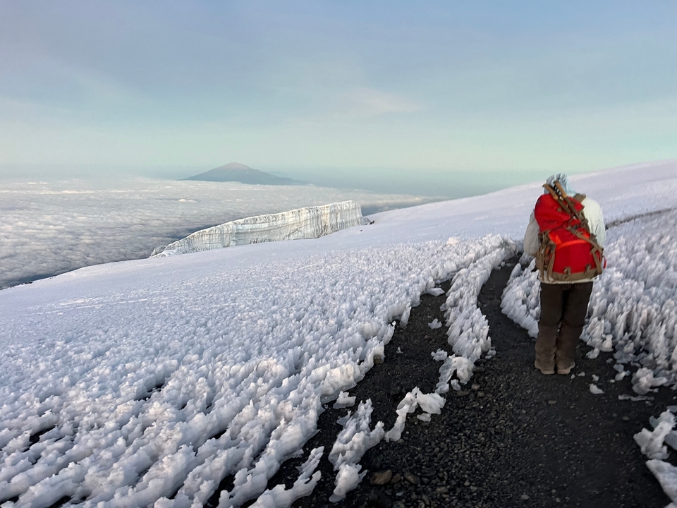 Sentier enneigé menant à un glacier avec une personne qui marche.