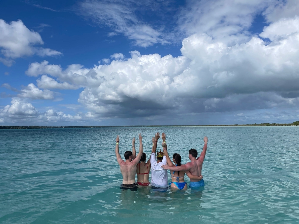 Groupe de personnes dans l'eau tournant le dos, avec un ciel nuageux