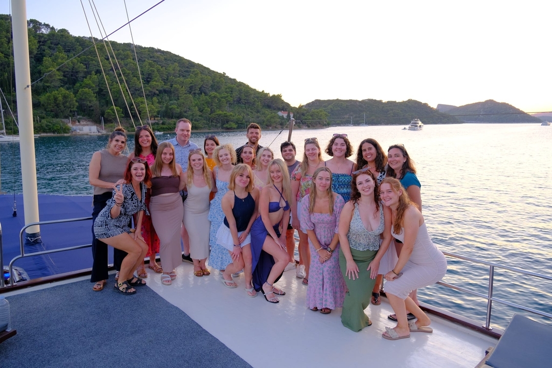 Large group of people posing on a boat at sunset.