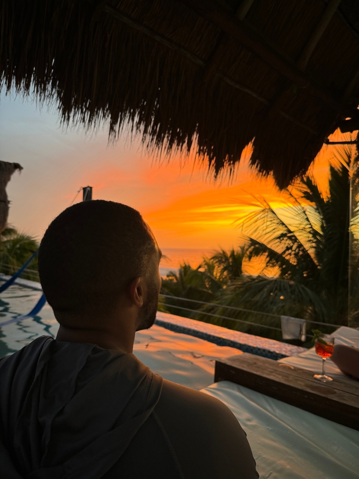 Personne contemplant un coucher de soleil vibrant sur l'océan avec des palmiers.