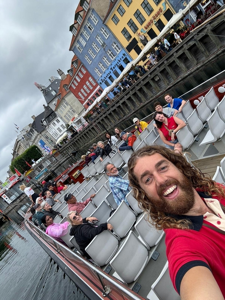 Un groupe de personnes sur un bateau touristique avec des bâtiments colorés le long du front de mer.