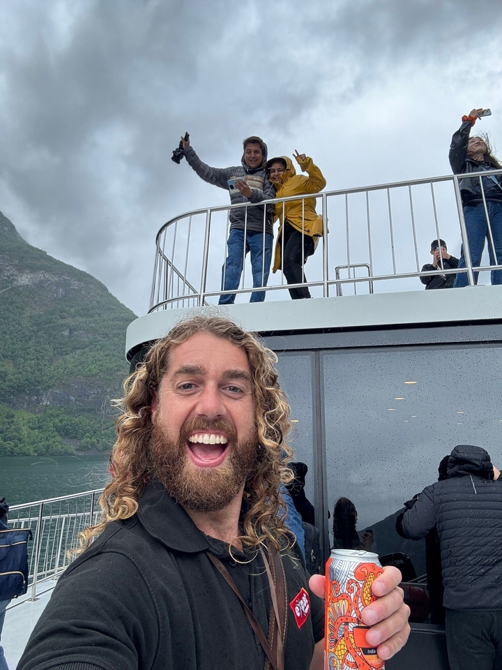 Un homme souriant sur un bateau avec des montagnes en arrière-plan.