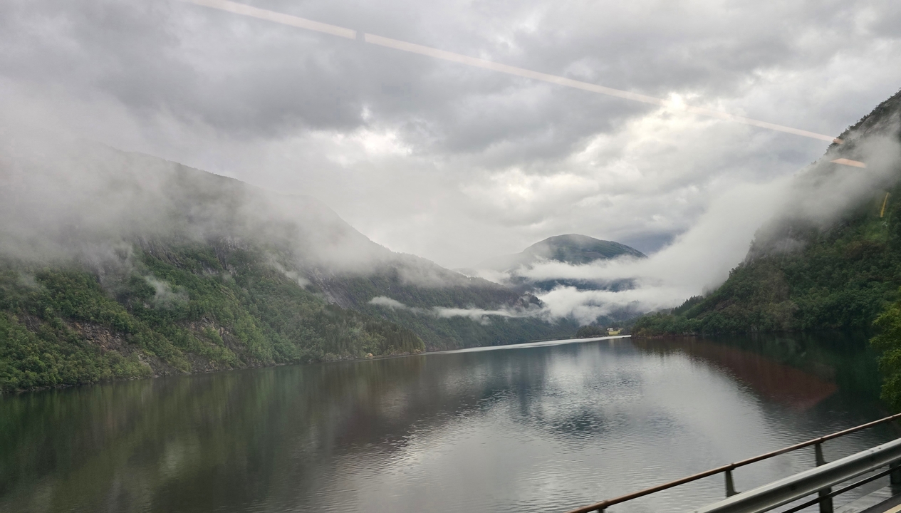 Paysage de montagne et de lac couvert de brume, se reflétant sur l'eau immobile.