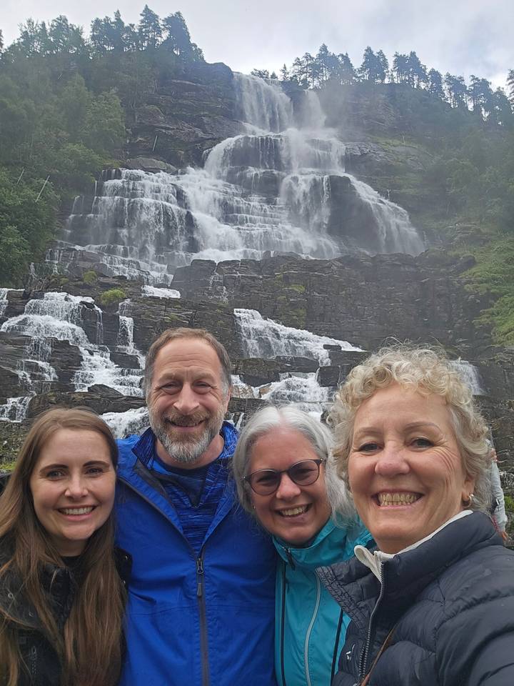 Quatre personnes souriantes devant une grande cascade.
