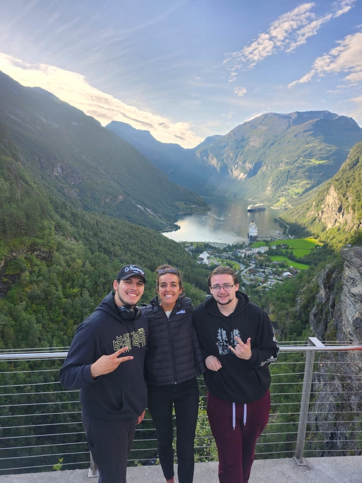 Trois personnes posant avec une vue panoramique sur un fjord et un navire de croisière en contrebas.