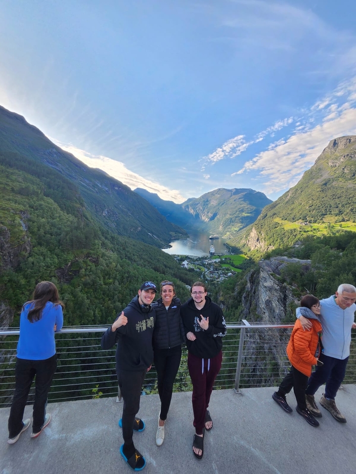 Trois personnes posant avec une vue panoramique sur un fjord et un navire de croisière en contrebas.