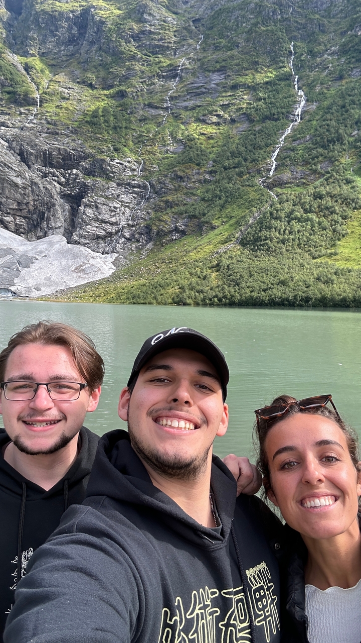 Trois personnes souriantes avec en arrière-plan une montagne rocheuse et un lac.