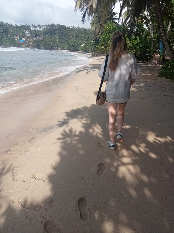Personne marchant le long d'une plage de sable avec des ombres d'arbres.