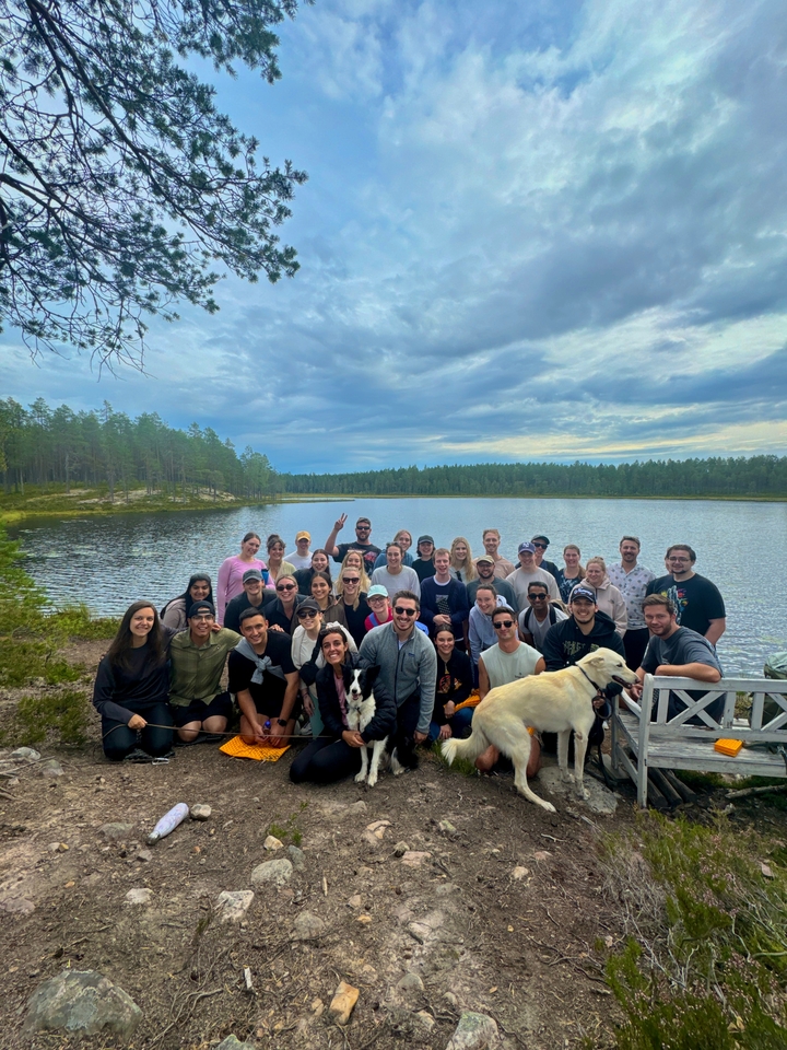 Large group of people posing by a lake in a forest.