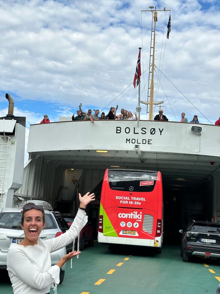 People waving from a ferry named BOLSØY with a travel bus below.