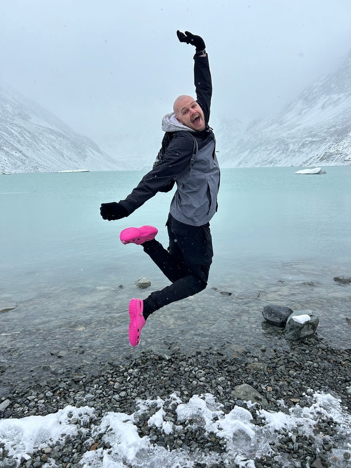 Personne sautant joyeusement devant un lac enneigé.