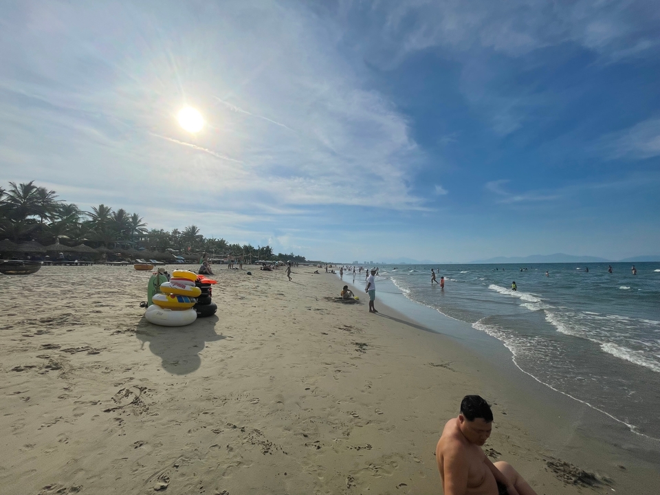 Plage avec des gens qui prennent un bain de soleil et nagent sous le soleil.