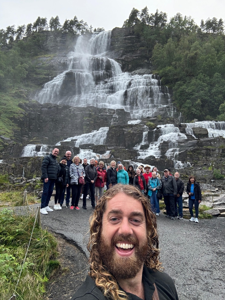 Groupe devant une grande cascade sur un terrain rocheux.
