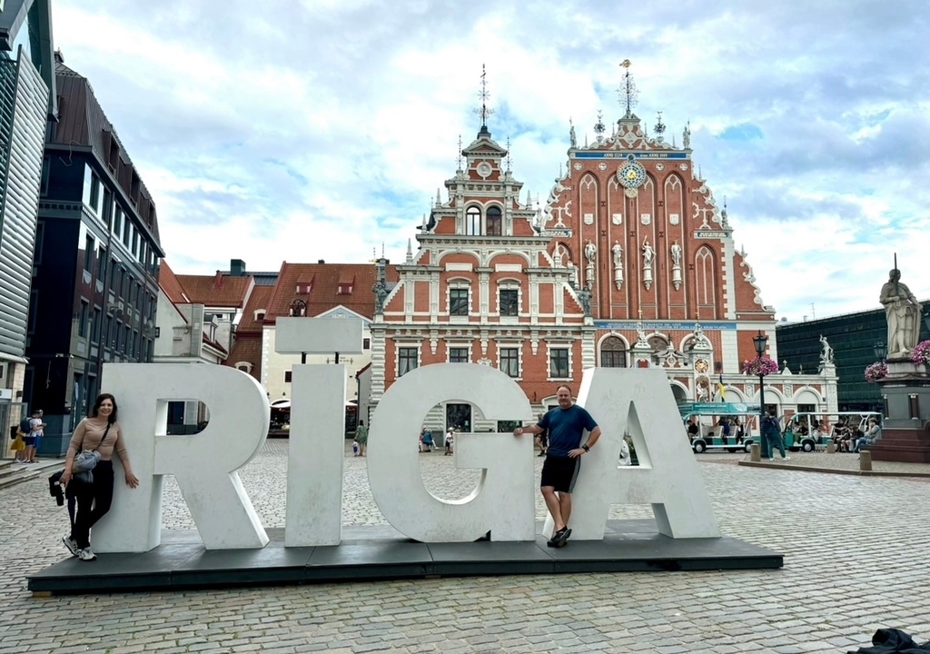 Des personnes posant avec de grandes lettres épelant 'RIGA' devant des bâtiments historiques.
