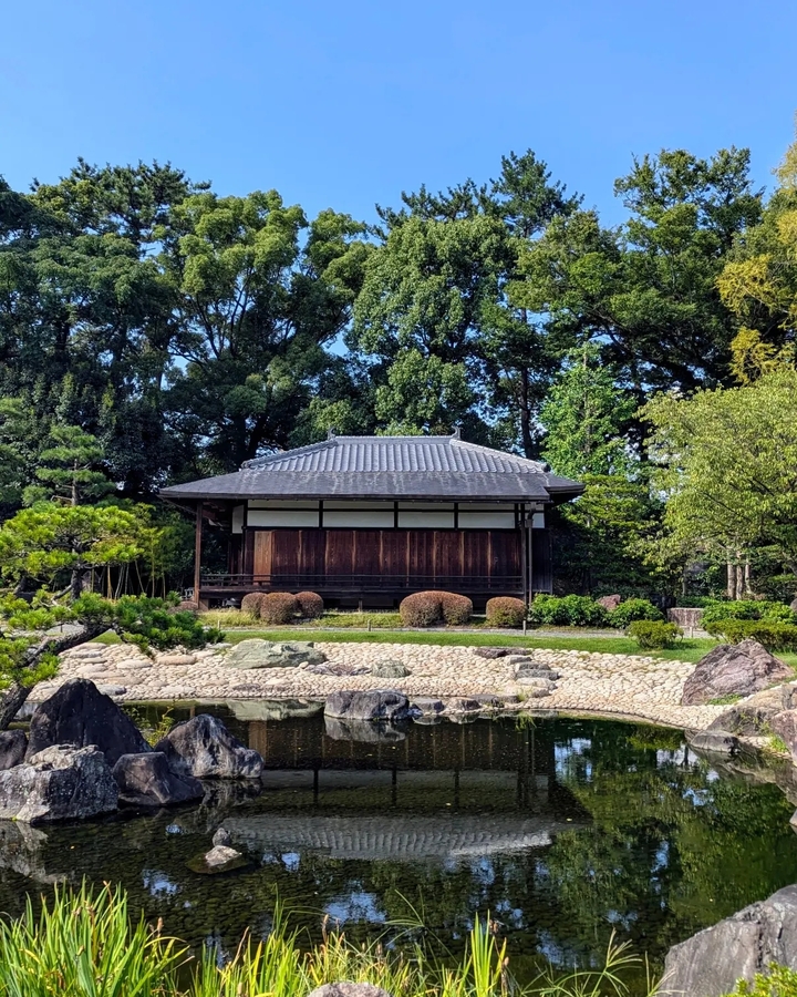 Maison japonaise traditionnelle entourée d'arbres et d'un jardin de rocaille.