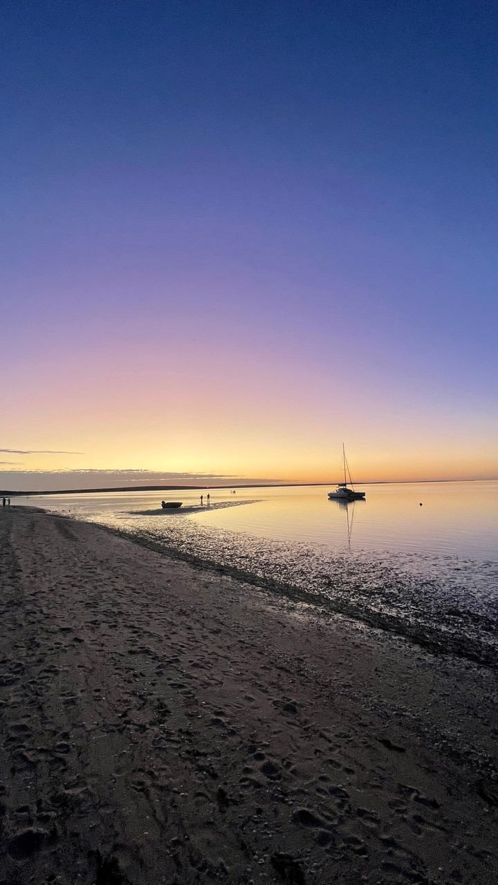 Coucher de soleil sur une mer calme avec des bateaux et des personnes en silhouette.