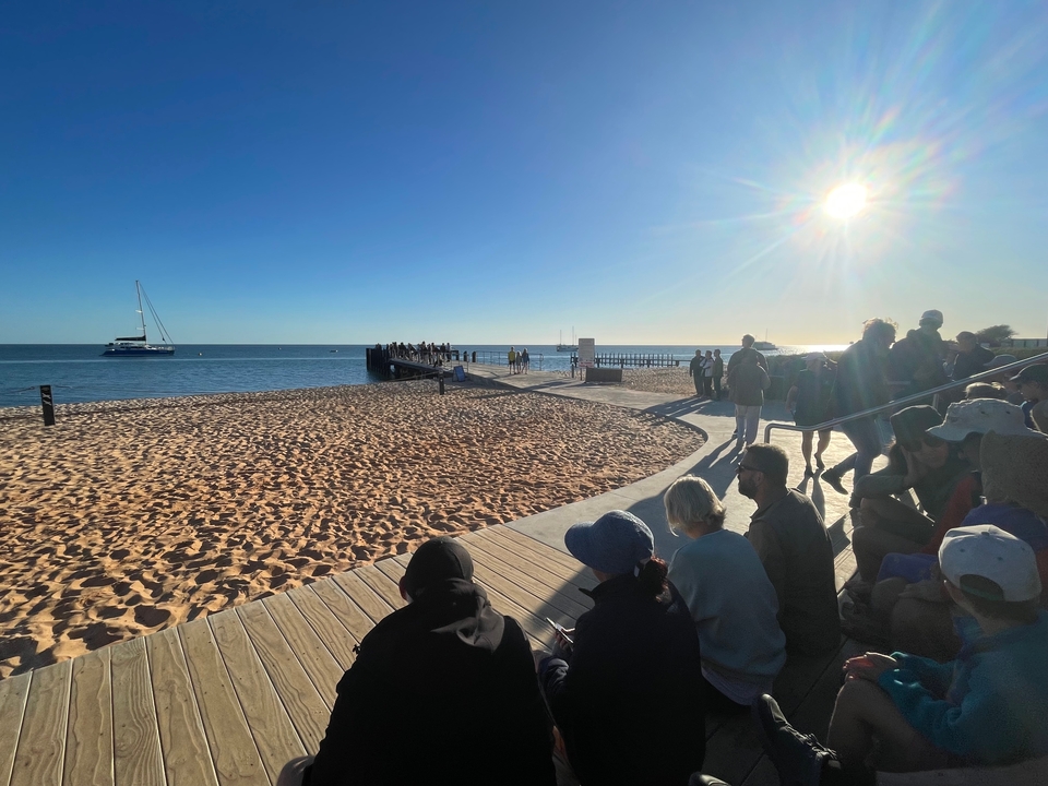 Des gens assis au bord de la plage regardant le soleil au-dessus de la mer.
