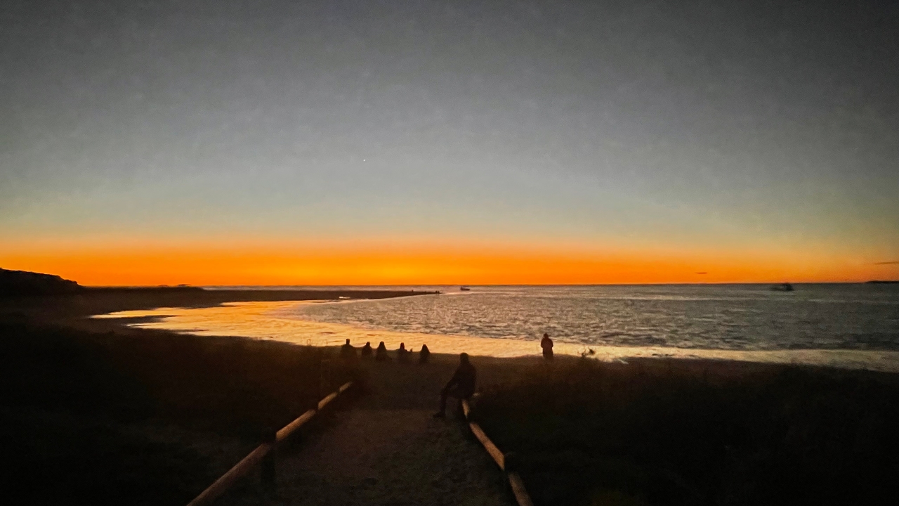 Des silhouettes de personnes assises à la plage pendant un coucher de soleil éclatant.