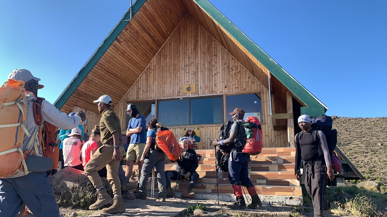 Des gens se sont rassemblés devant une cabane en bois au pied d'une montagne.