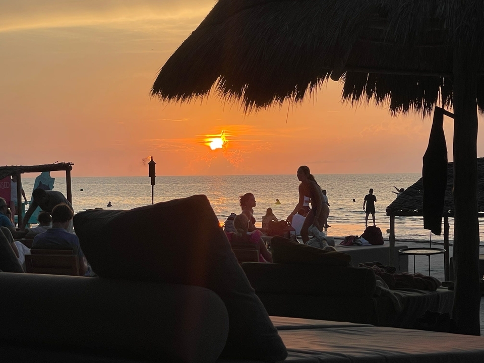 Une scène de plage au coucher du soleil avec des silhouettes de personnes et de chaises longues.