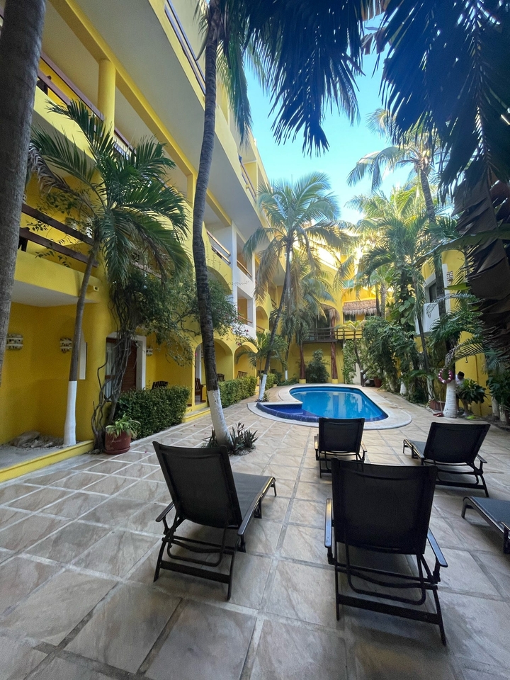 Une cour avec une piscine entourée de murs jaunes et de plantes tropicales.