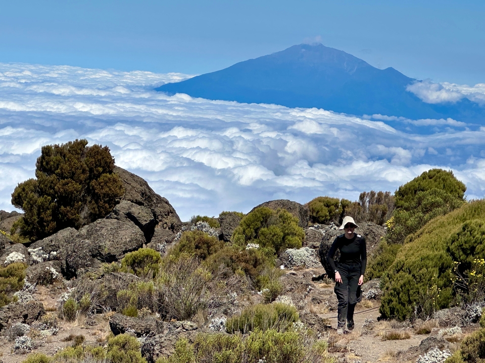 Randonneur gravissant un sentier avec une vue montagneuse au-dessus des nuages.