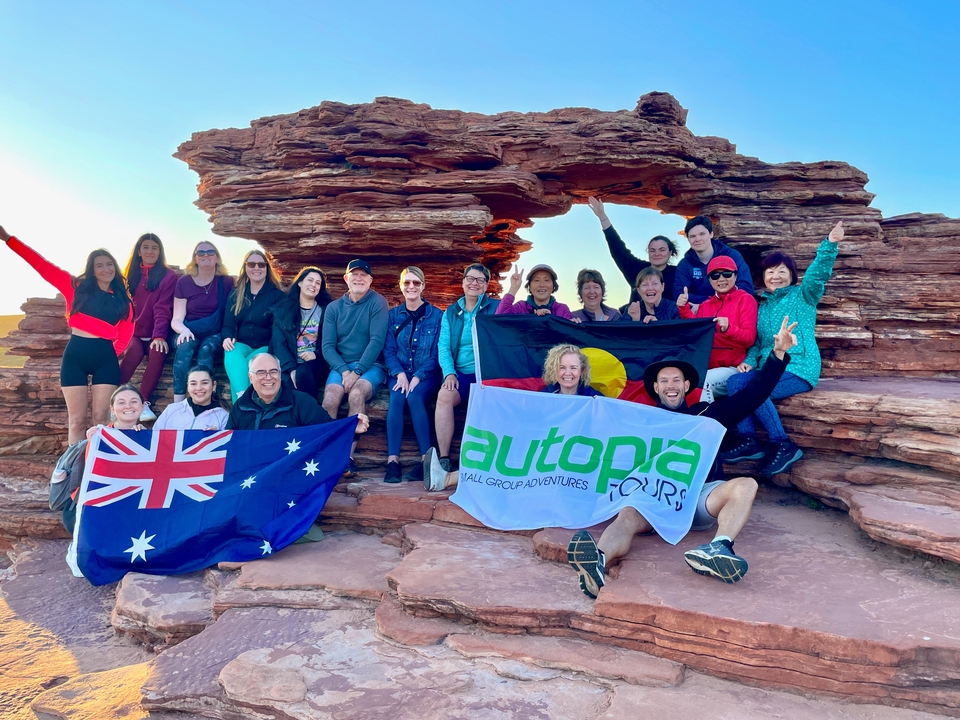 Groupe de personnes posant avec des drapeaux australiens dans une zone rocheuse.