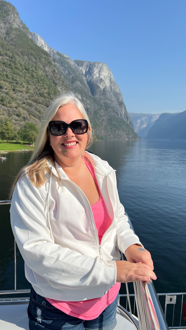 Personne souriante avec un fjord et des montagnes en arrière-plan.