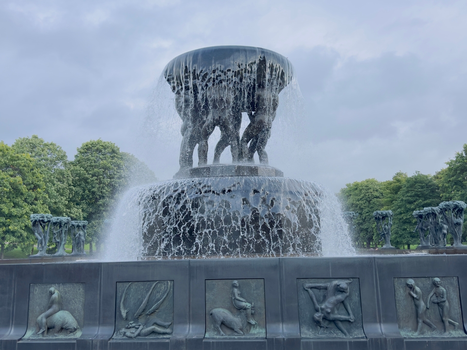 Une grande fontaine avec des sculptures complexes, entourée de verdure.
