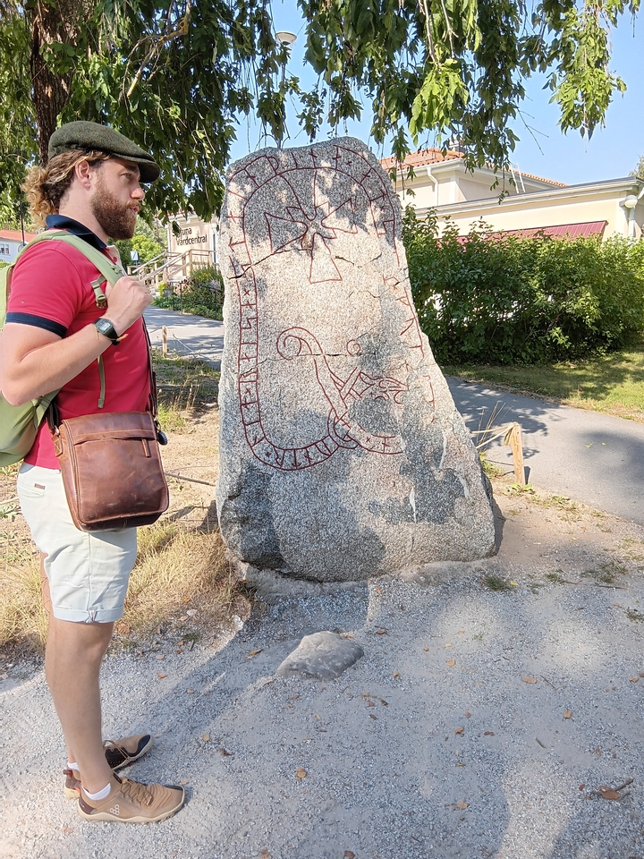 Personne debout à côté d'une pierre runique avec des gravures par une journée ensoleillée.