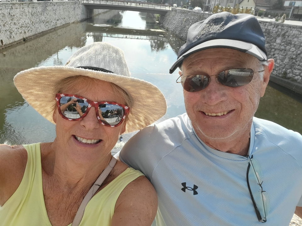 Selfie de deux personnes avec des lunettes de soleil et des chapeaux au bord d'une rivière.