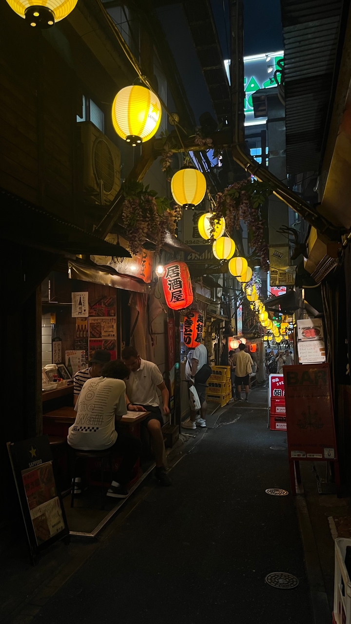 Ruelle animée avec des lanternes colorées et des enseignes la nuit.
