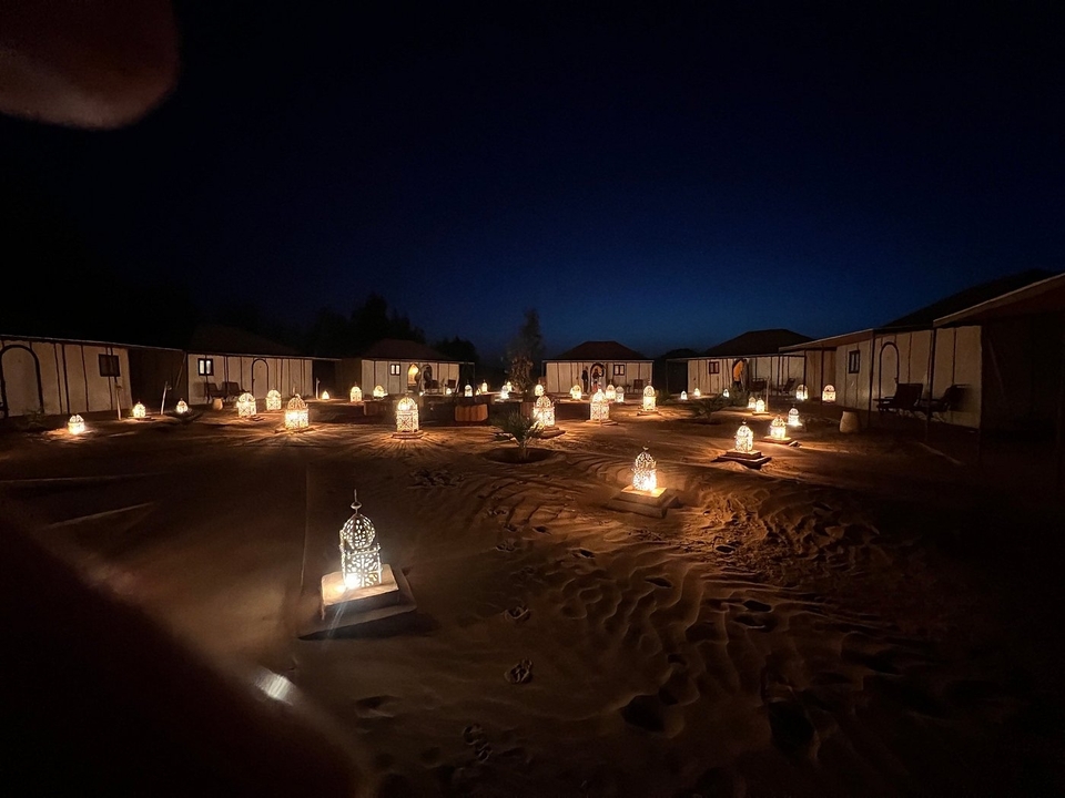 Campement nocturne dans le désert avec des lanternes illuminant les tentes.