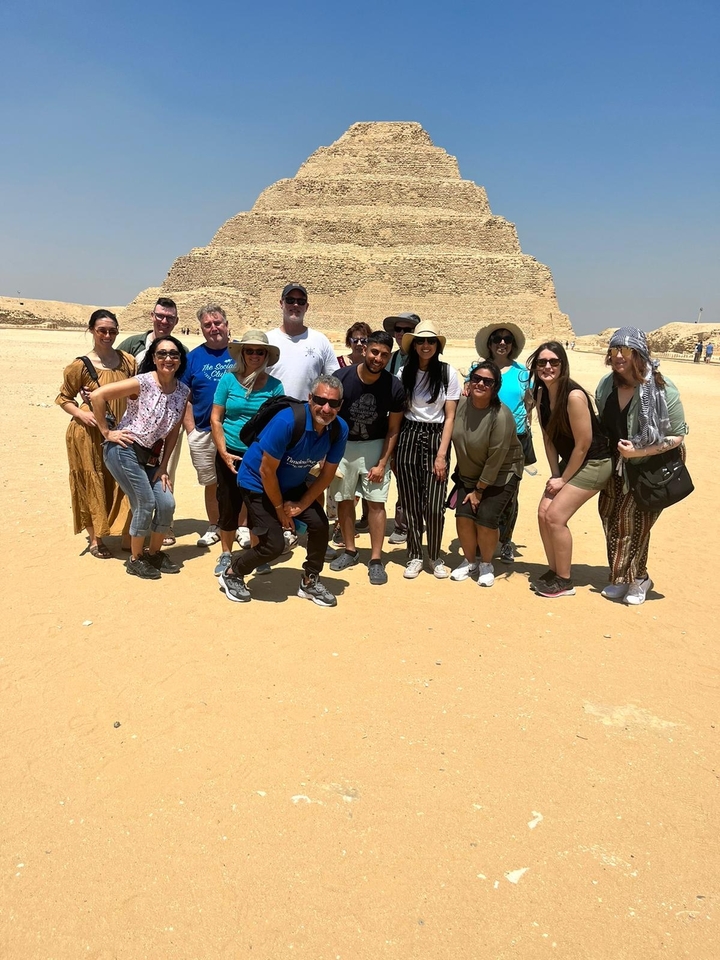 Un groupe de touristes posant devant une pyramide sous un ciel dégagé.
