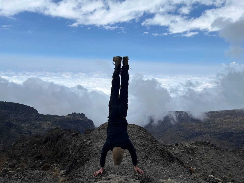 Personne faisant le poirier sur un paysage montagneux au-dessus des nuages.