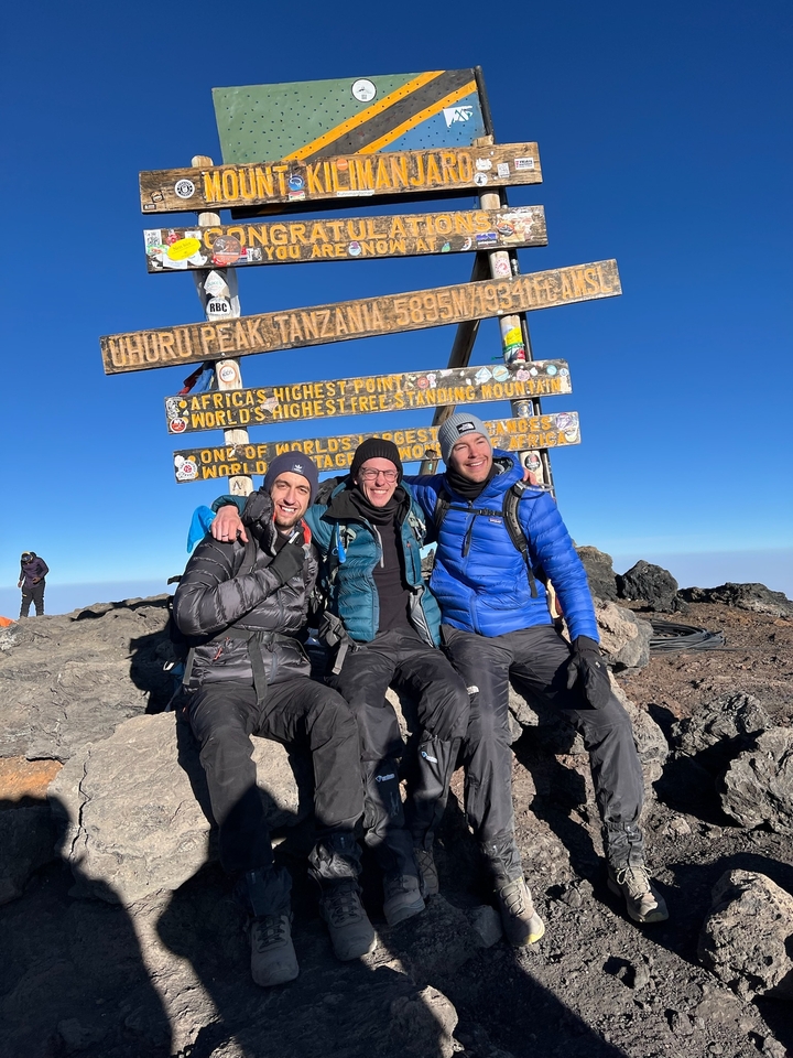 Trois personnes qui posent devant un panneau indiquant « Uhuru Peak, Tanzania ».