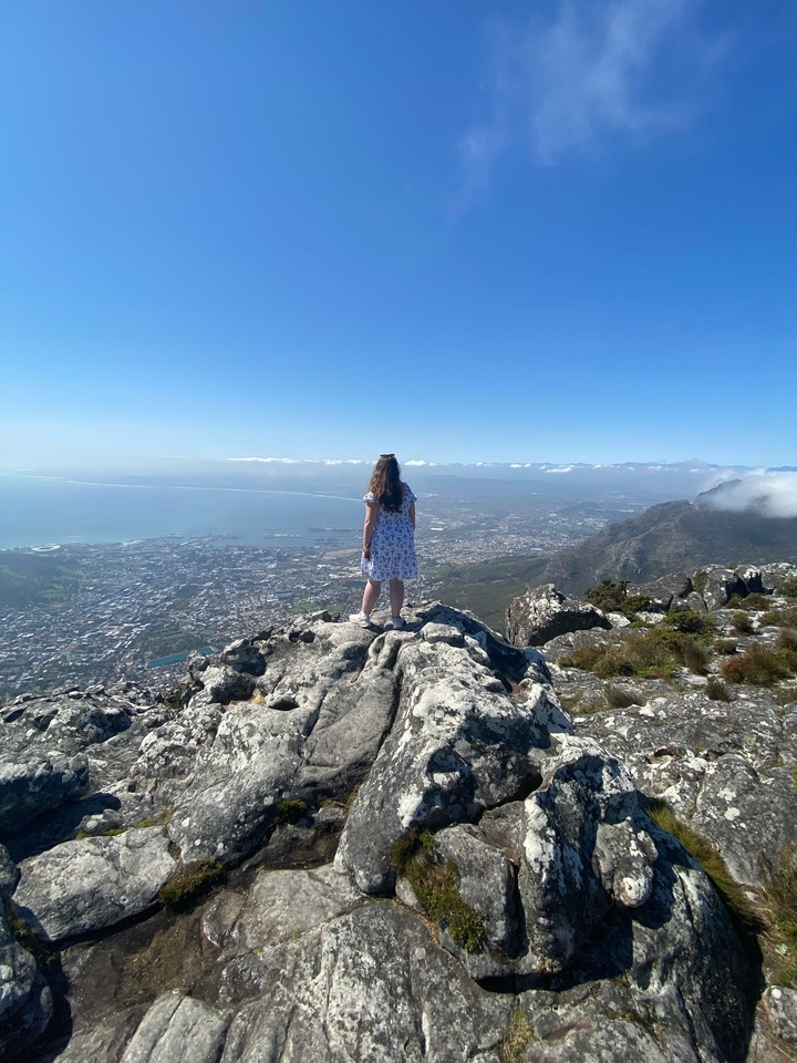 Personne debout au bord d'une falaise surplombant une ville et l'océan.