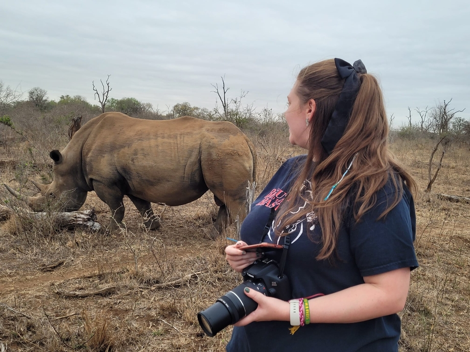 Femme tenant un appareil photo en observant un rhinocéros.