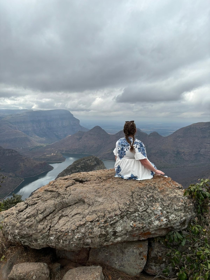 Femme assise sur un rocher surplombant un vaste paysage avec une rivière.