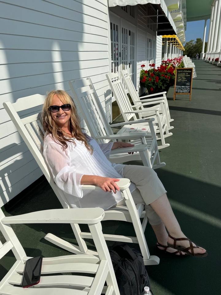 Femme assise sur une chaise berçante blanche sur une terrasse.