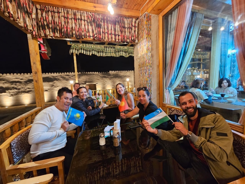Grupo de personas en un restaurante sosteniendo banderas de Kazajstán y Uzbekistán.