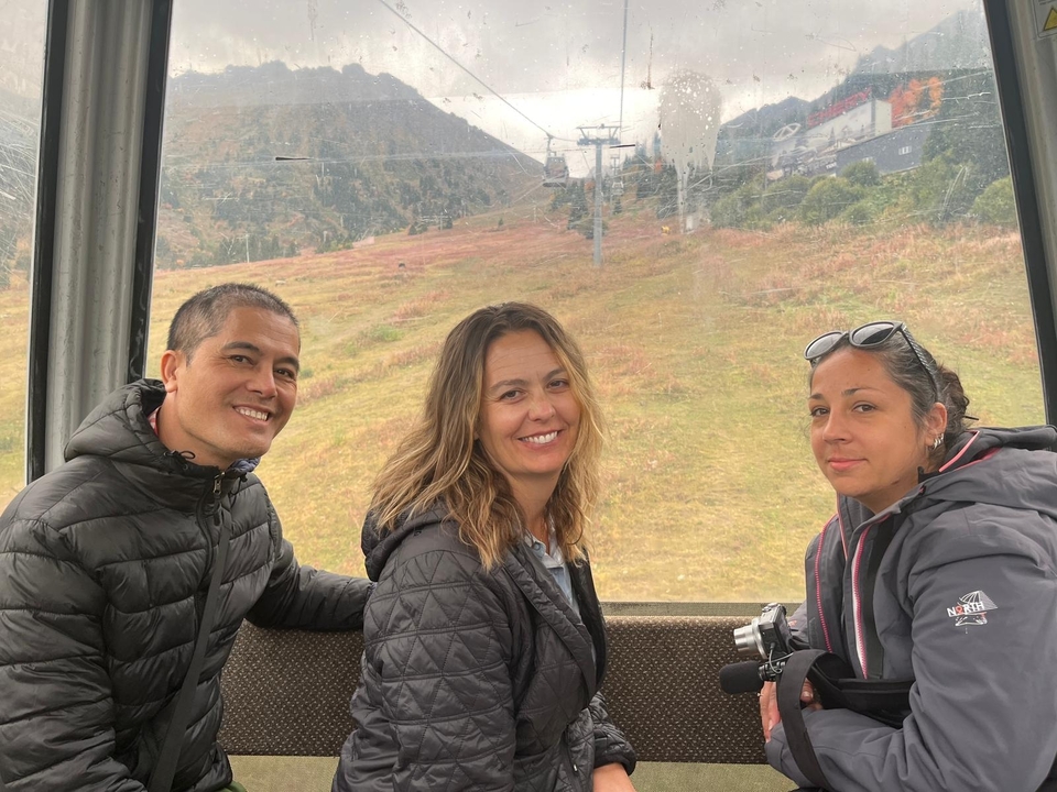 Tres personas dentro de un teleférico con montañas al fondo.