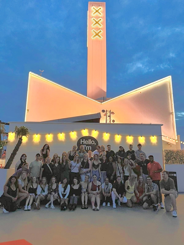 Grand groupe de personnes posant devant un bâtiment avec des guirlandes lumineuses.